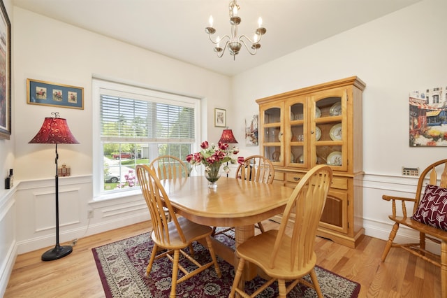 dining area with light wood-style floors, a chandelier, wainscoting, and a decorative wall