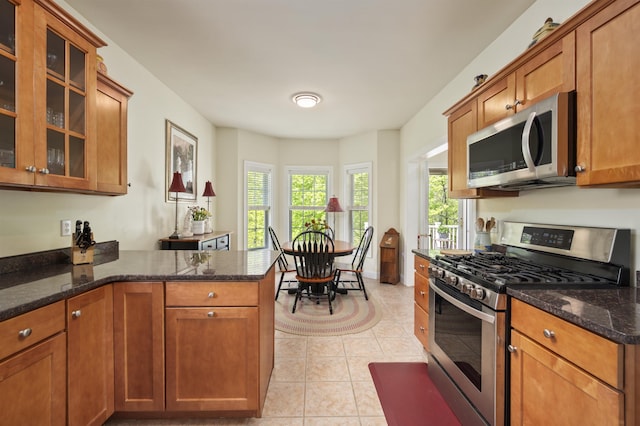 kitchen with stainless steel appliances, brown cabinets, a peninsula, and dark stone countertops