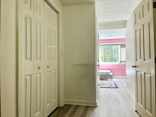 corridor with wood finished floors, baseboards, and a textured ceiling