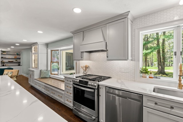 kitchen featuring appliances with stainless steel finishes, custom exhaust hood, a sink, light stone counters, and decorative backsplash