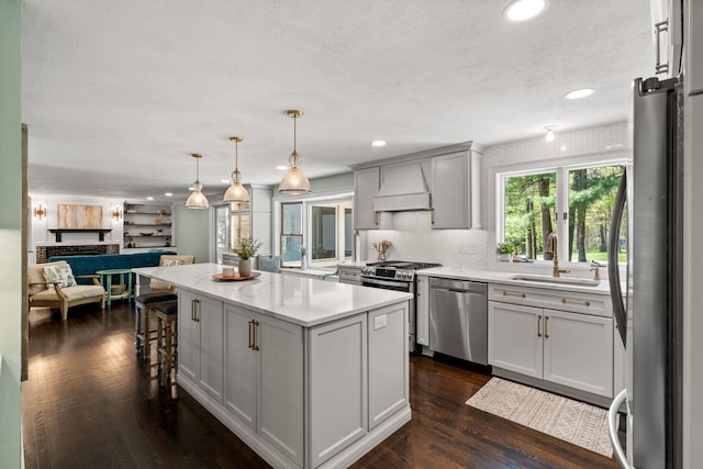 kitchen with stainless steel appliances, custom range hood, a sink, a textured ceiling, and a kitchen island