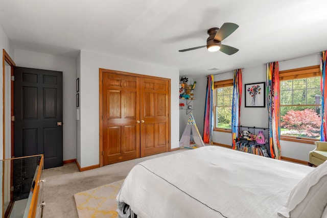 bedroom with a closet, baseboards, light colored carpet, and a ceiling fan