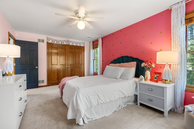 bedroom with wallpapered walls, multiple windows, light carpet, a closet, and a ceiling fan