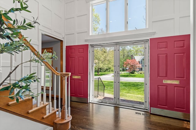 foyer featuring a high ceiling, stairway, a decorative wall, plenty of natural light, and dark wood-style floors