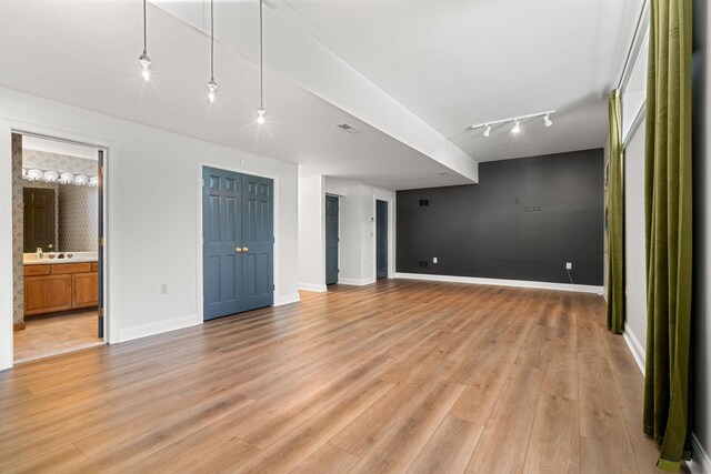 unfurnished living room with light wood-type flooring, track lighting, baseboards, and a sink
