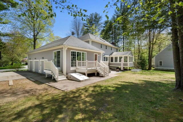 rear view of property featuring a sunroom, a lawn, a deck, and a shingled roof