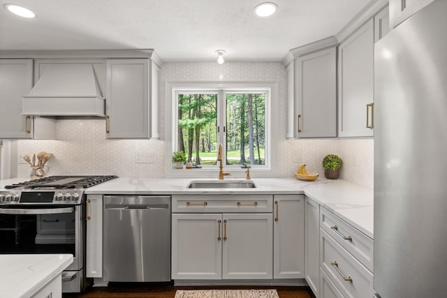 kitchen with stainless steel appliances, a sink, custom range hood, backsplash, and light stone countertops