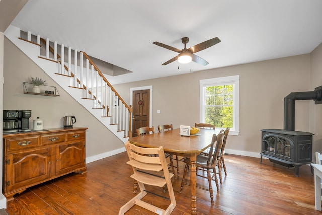 dining room featuring stairway, ceiling fan, a wood stove, dark wood-type flooring, and baseboards
