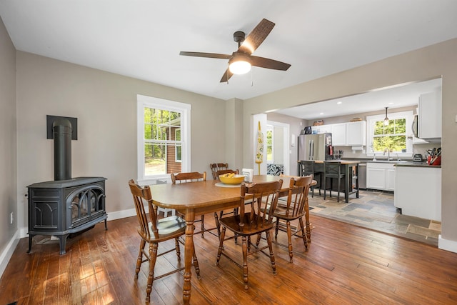 dining space with hardwood / wood-style floors, ceiling fan, a wood stove, and baseboards