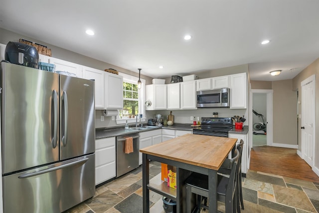 kitchen featuring stainless steel appliances, dark countertops, a sink, white cabinetry, and dark stone finish floors