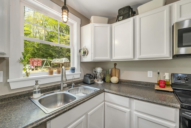 kitchen featuring a sink, stainless steel microwave, white cabinets, and dark countertops