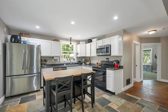 kitchen with appliances with stainless steel finishes, butcher block counters, a sink, white cabinetry, and recessed lighting