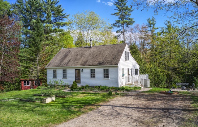 cape cod home with a front yard, an outbuilding, roof with shingles, a vegetable garden, and driveway