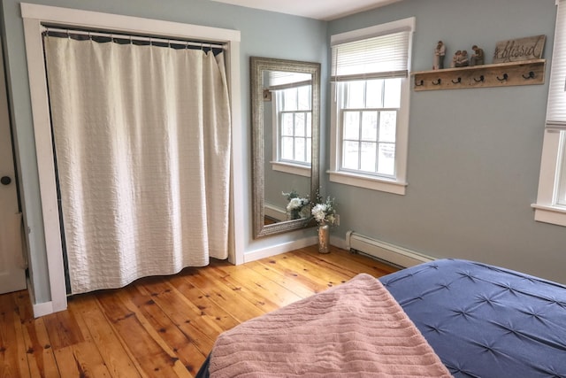 bedroom with a baseboard heating unit, hardwood / wood-style floors, and baseboards