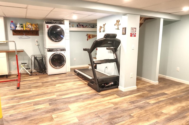 washroom with stacked washing machine and dryer, wood finished floors, and baseboards