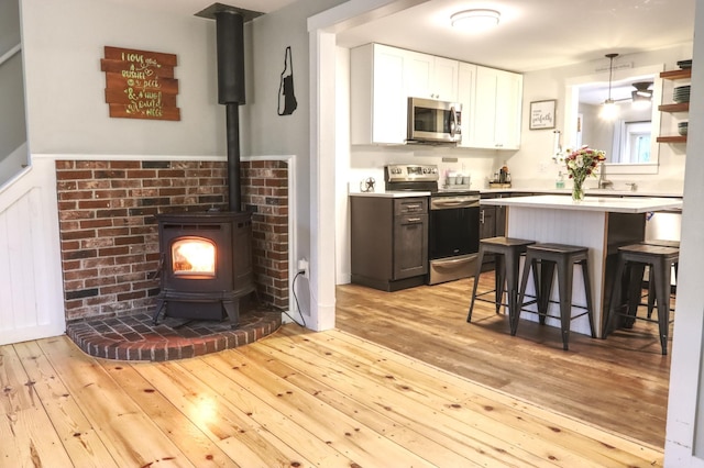 kitchen featuring stainless steel appliances, a kitchen breakfast bar, a wood stove, light wood-style floors, and light countertops
