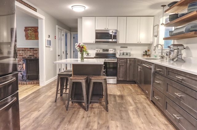 kitchen featuring stainless steel appliances, a sink, a kitchen bar, white cabinetry, and a wood stove