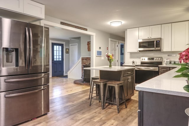 kitchen with appliances with stainless steel finishes, light wood-style flooring, white cabinets, and light stone counters