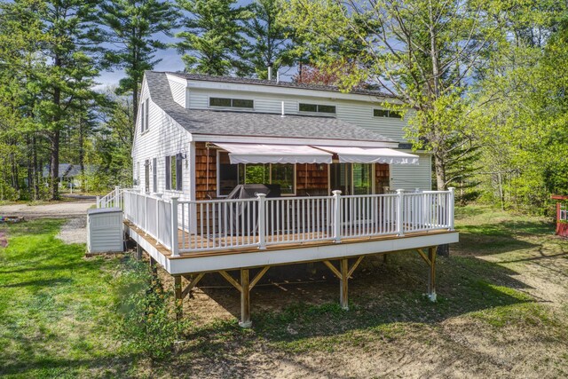 view of front of house featuring roof with shingles, a deck, and a front yard