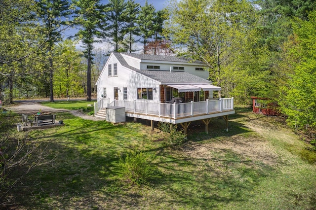 rear view of property with a shingled roof, a wooden deck, and a lawn