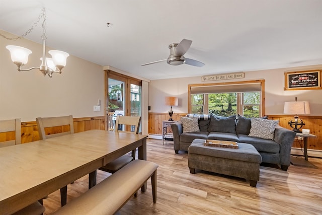 living area featuring a wainscoted wall, light wood-style floors, a chandelier, a baseboard heating unit, and wood walls