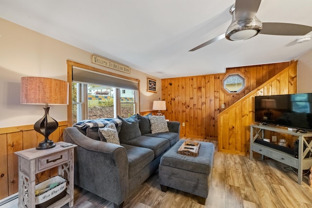 living area with wooden walls, ceiling fan, and light wood-style flooring