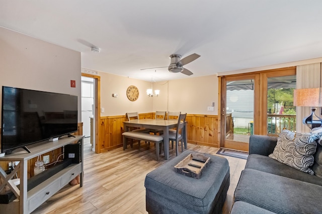 living room featuring wainscoting, light wood-type flooring, a ceiling fan, a chandelier, and wooden walls