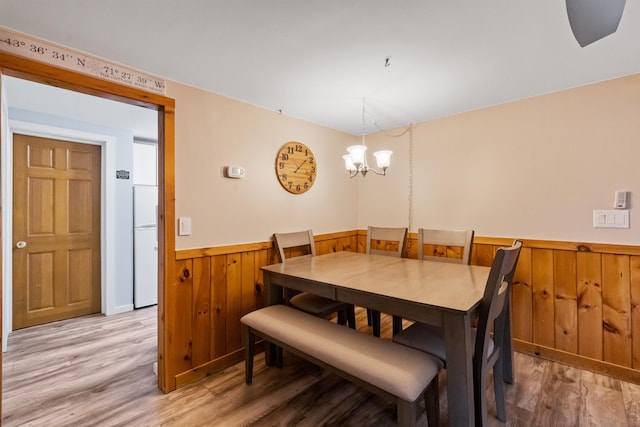 dining area with wainscoting, wooden walls, light wood-style floors, and a chandelier