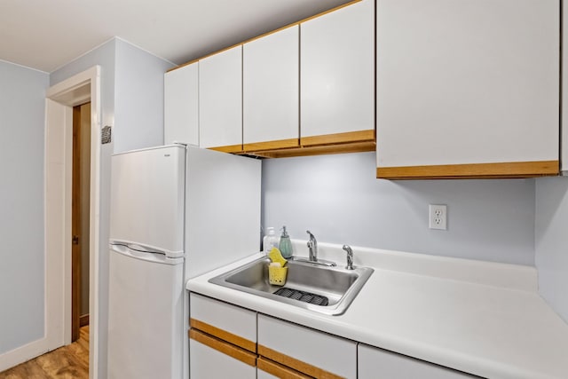 kitchen with a sink, freestanding refrigerator, white cabinetry, light countertops, and light wood finished floors