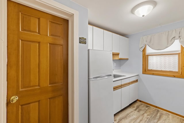 kitchen featuring freestanding refrigerator, white cabinets, light countertops, baseboards, and light wood-style floors
