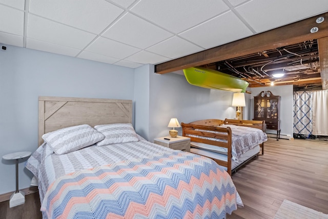 bedroom with baseboard heating, wood finished floors, and a drop ceiling