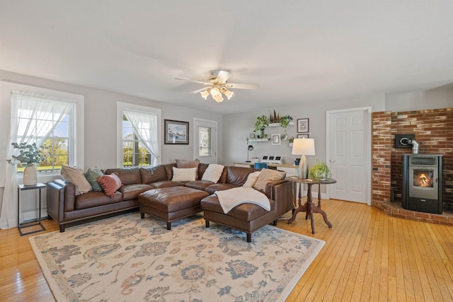 living area with light wood finished floors, a wood stove, and ceiling fan