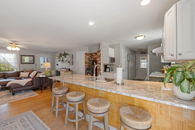 kitchen featuring a sink, stainless steel microwave, a peninsula, white cabinets, and a ceiling fan
