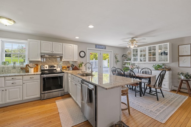 kitchen with appliances with stainless steel finishes, a sink, under cabinet range hood, a peninsula, and light wood-style floors
