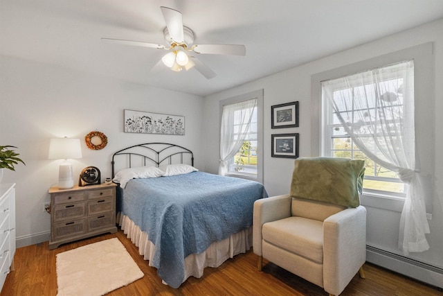 bedroom featuring a baseboard radiator, multiple windows, wood finished floors, and ceiling fan