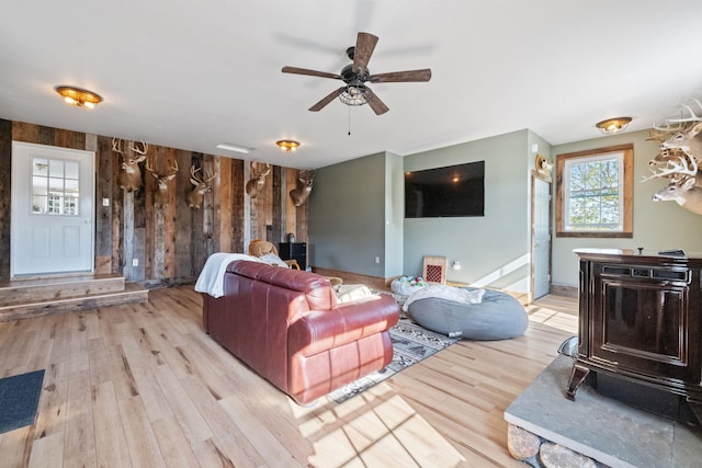 living room with wood finished floors, a wood stove, wooden walls, and ceiling fan
