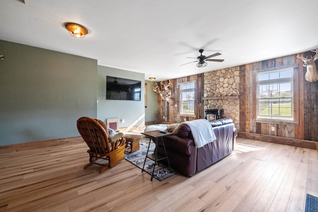 living room with plenty of natural light, wood finished floors, ceiling fan, and a stone fireplace