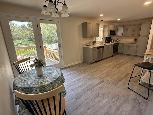 kitchen with stainless steel appliances, a sink, gray cabinets, a chandelier, and light countertops