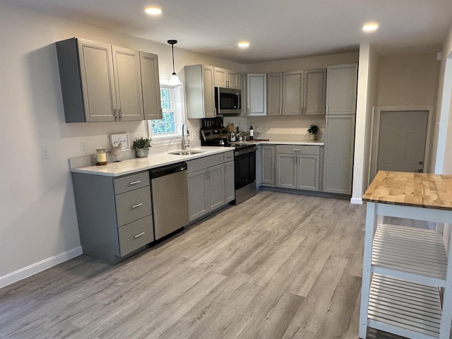 kitchen with appliances with stainless steel finishes, a sink, gray cabinetry, light wood-type flooring, and recessed lighting