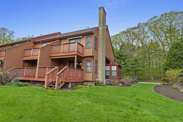back of house with a chimney, a lawn, a balcony, and a wooden deck