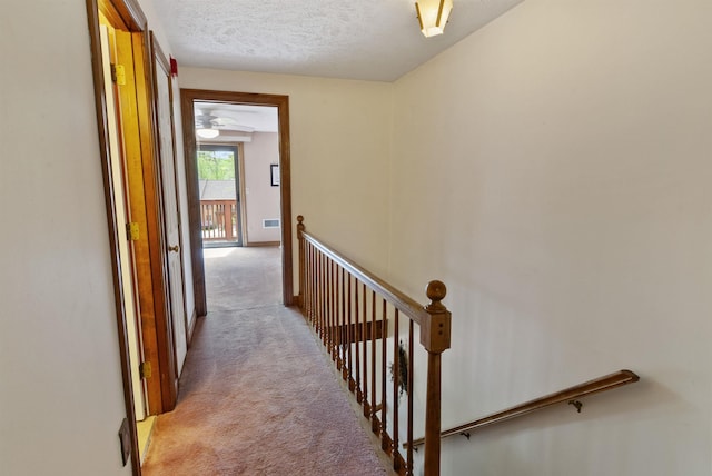 corridor featuring light colored carpet, an upstairs landing, and a textured ceiling