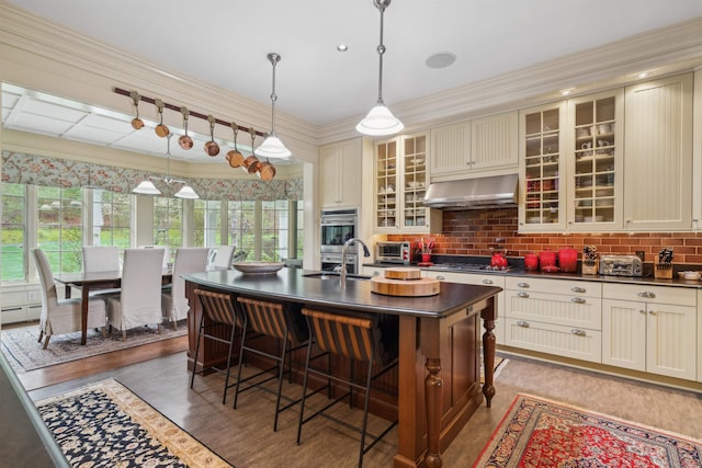 5893 Stage Rd, Barnard, VT 05031 - kitchen with exhaust hood, dark countertops, cream cabinetry, a sink, and a kitchen breakfast bar