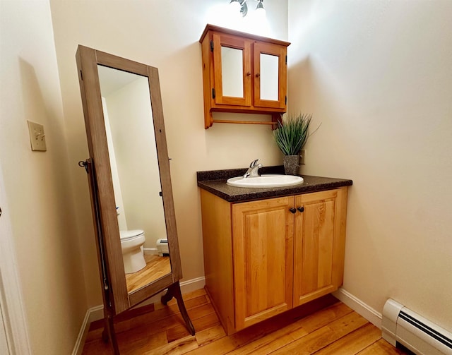 half bath with baseboard heating, toilet, vanity, wood finished floors, and baseboards