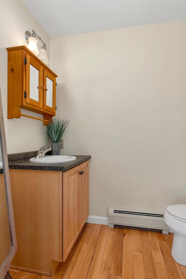 bathroom with hardwood / wood-style flooring, baseboard heating, vanity, toilet, and baseboards