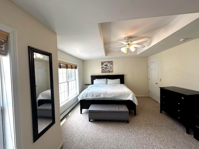bedroom featuring a baseboard heating unit, light colored carpet, baseboards, a tray ceiling, and a ceiling fan