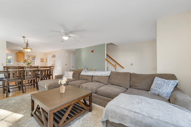 living area with a ceiling fan, light wood finished floors, and stairway