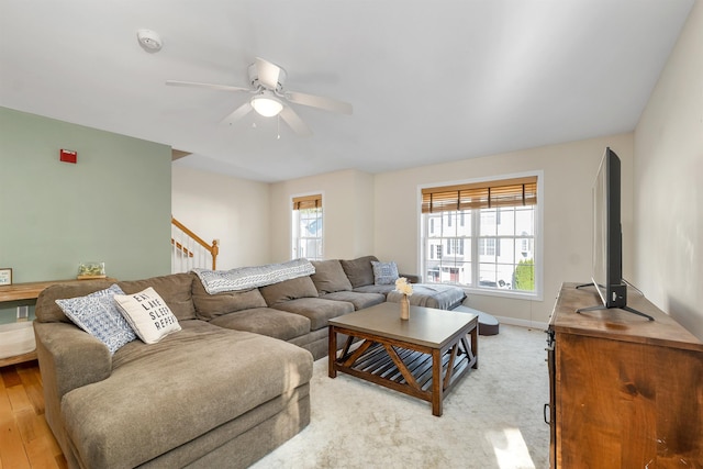 living area with a ceiling fan, baseboards, stairway, and light wood-type flooring