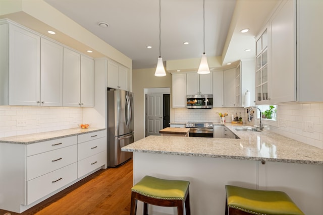 kitchen with stainless steel appliances, a sink, a peninsula, tasteful backsplash, and recessed lighting