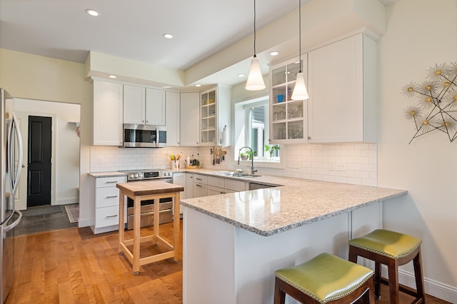 kitchen with stainless steel appliances, a sink, a peninsula, light wood-style floors, and glass insert cabinets