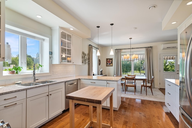 kitchen with a sink, a wall mounted AC, a peninsula, light wood-style flooring, and white cabinetry
